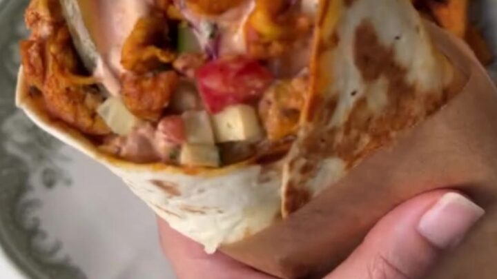 Crispy chicken shawarma wrap cut in half, showing layers of chicken, fries, and pickled turnips, with garlic sauce.