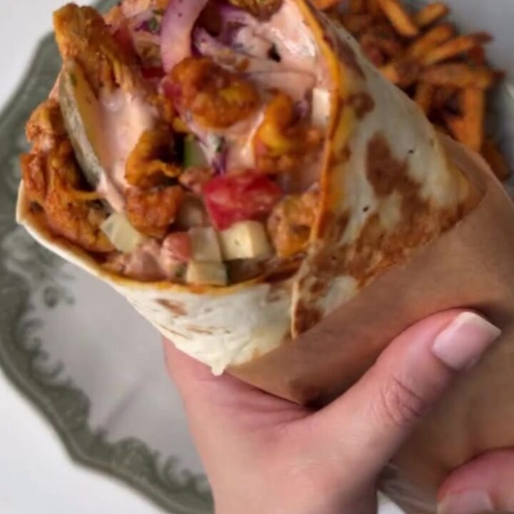 Crispy chicken shawarma wrap cut in half, showing layers of chicken, fries, and pickled turnips, with garlic sauce.
