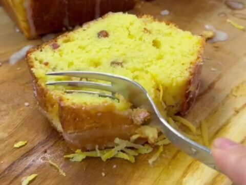 Golden whole-lemon loaf cake with glossy lemon glaze and a slice cut to show the moist crumb