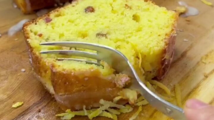 Golden whole-lemon loaf cake with glossy lemon glaze and a slice cut to show the moist crumb