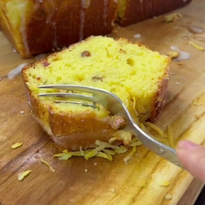 Golden whole-lemon loaf cake with glossy lemon glaze and a slice cut to show the moist crumb