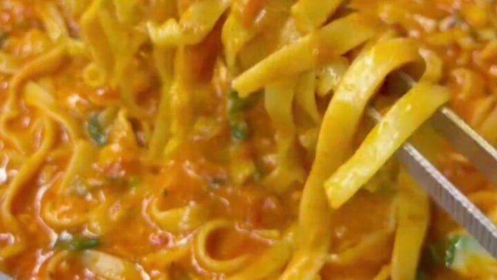 A fork twirling spaghetti with cherry tomatoes, zucchini, and melted parmesan in a skillet