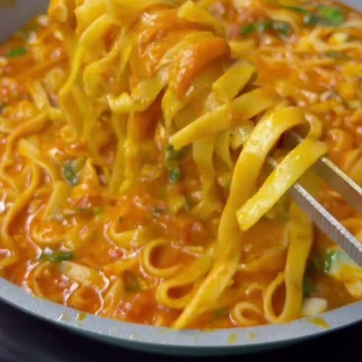 A fork twirling spaghetti with cherry tomatoes, zucchini, and melted parmesan in a skillet