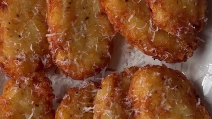 Golden crispy hashbrown patty with parmesan crust, broken in half showing fluffy interior, on a plate.