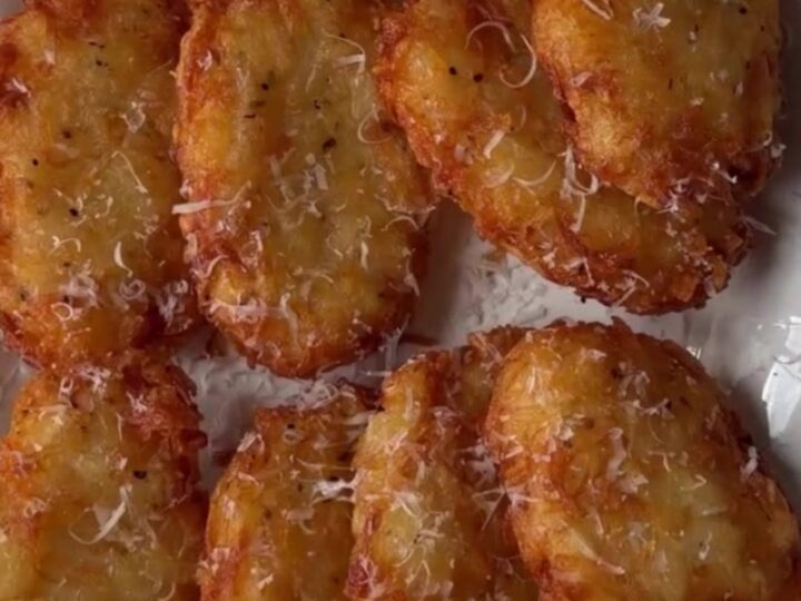 Golden crispy hashbrown patty with parmesan crust, broken in half showing fluffy interior, on a plate.