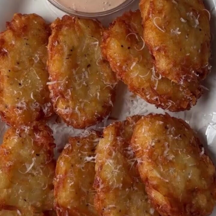 Golden crispy hashbrown patty with parmesan crust, broken in half showing fluffy interior, on a plate.