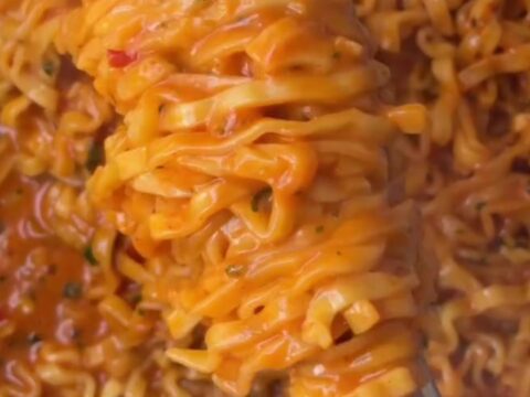 Glossy wavy ramen noodles coated in spicy garlic chili oil sauce, garnished with red chilies and green onions