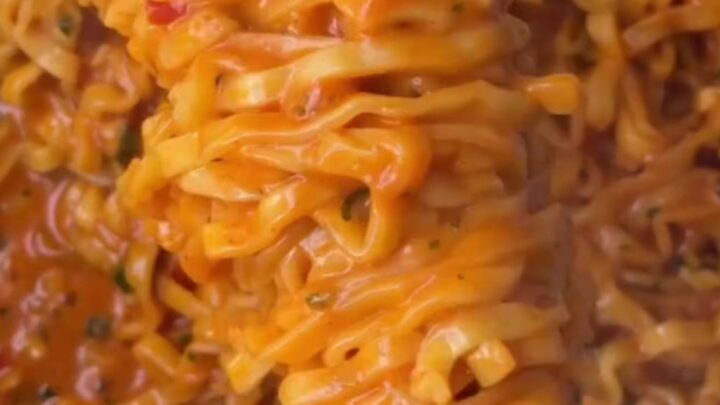 Glossy wavy ramen noodles coated in spicy garlic chili oil sauce, garnished with red chilies and green onions