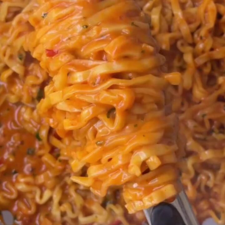 Glossy wavy ramen noodles coated in spicy garlic chili oil sauce, garnished with red chilies and green onions