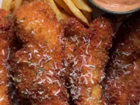 Crispy garlic parmesan chicken tenders with a creamy sweet chili dip in a small bowl, golden and crunchy.