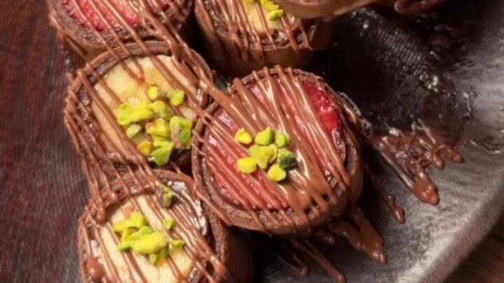 Chocolate crepe sushi pieces arranged on a plate, drizzled with white chocolate and sprinkled with pistachios.