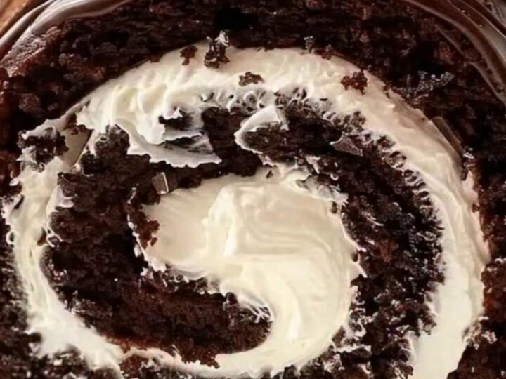 A decadent chocolate cake roll sliced to reveal a perfect white whipped cream swirl on a white platter.