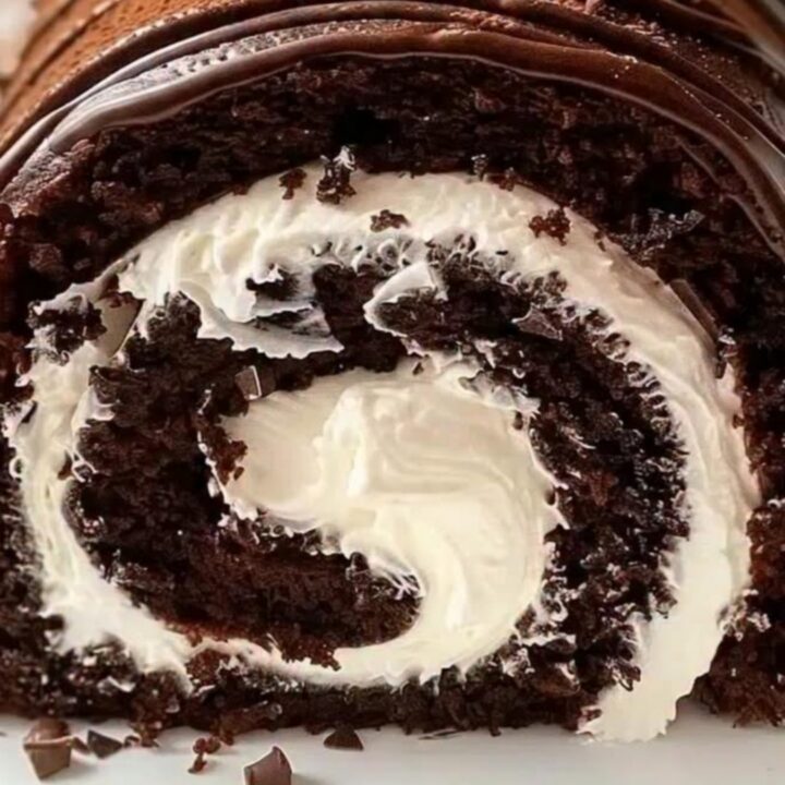 A decadent chocolate cake roll sliced to reveal a perfect white whipped cream swirl on a white platter.