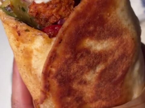 A crispy chicken shish kebab wrap sliced diagonally, showing juicy chicken and charred peppers