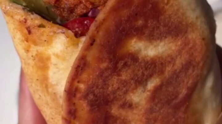 A crispy chicken shish kebab wrap sliced diagonally, showing juicy chicken and charred peppers