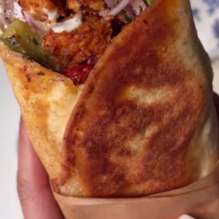 A crispy chicken shish kebab wrap sliced diagonally, showing juicy chicken and charred peppers