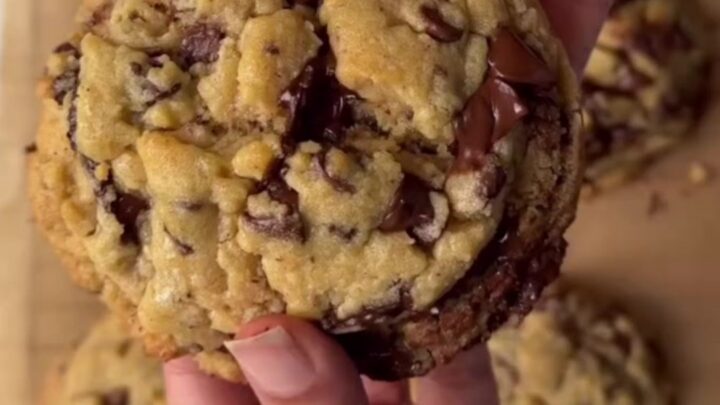 A tall chocolate chip cookie broken in half, showing a gooey, fudgy center with melted chocolate stretching.