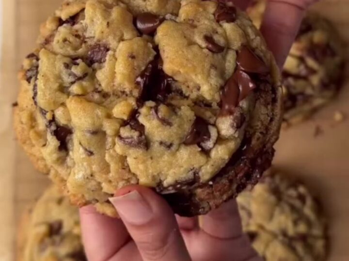 A tall chocolate chip cookie broken in half, showing a gooey, fudgy center with melted chocolate stretching.