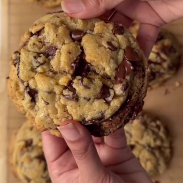 A tall chocolate chip cookie broken in half, showing a gooey, fudgy center with melted chocolate stretching.