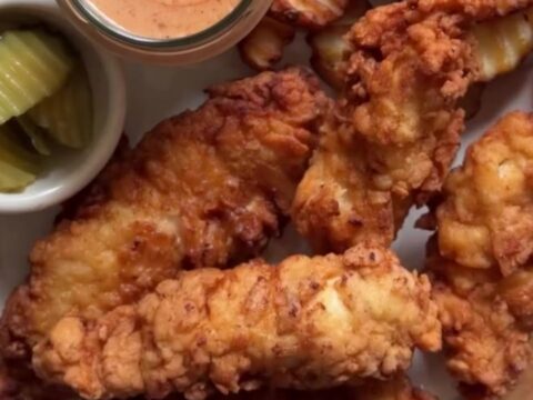 Golden crispy chicken fingers on a wire rack with a bowl of pink-orange sauce for dipping