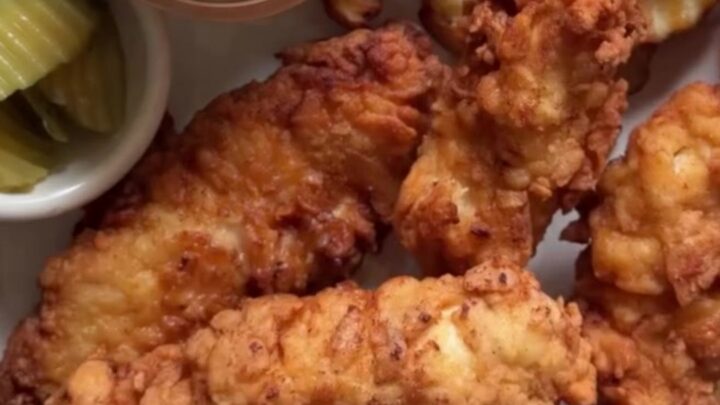 Golden crispy chicken fingers on a wire rack with a bowl of pink-orange sauce for dipping