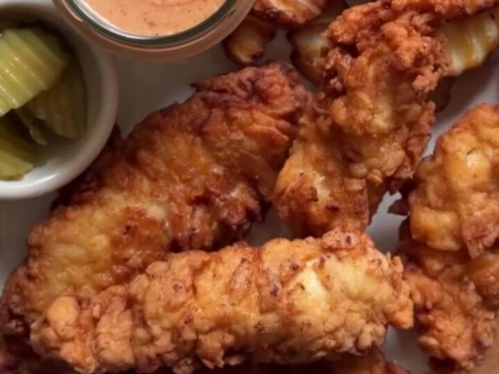 Golden crispy chicken fingers on a wire rack with a bowl of pink-orange sauce for dipping