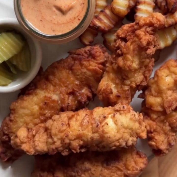 Golden crispy chicken fingers on a wire rack with a bowl of pink-orange sauce for dipping
