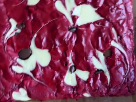 A fudgy red velvet cheesecake brownie slice showing marbled crimson and creamy layers on a white plate.