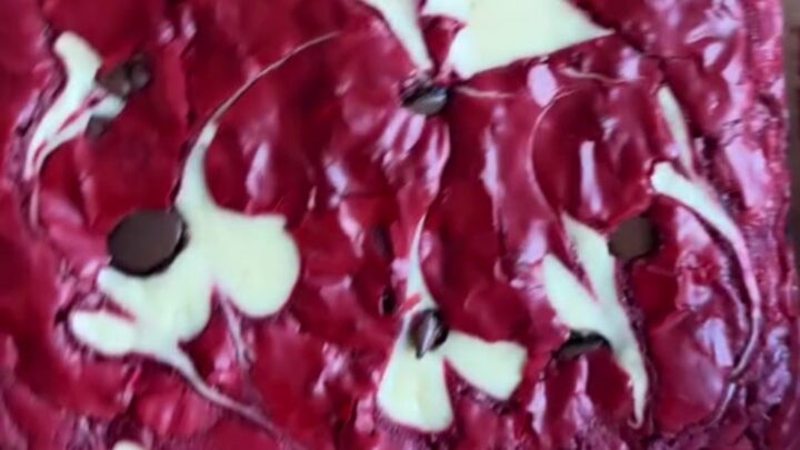 A fudgy red velvet cheesecake brownie slice showing marbled crimson and creamy layers on a white plate.