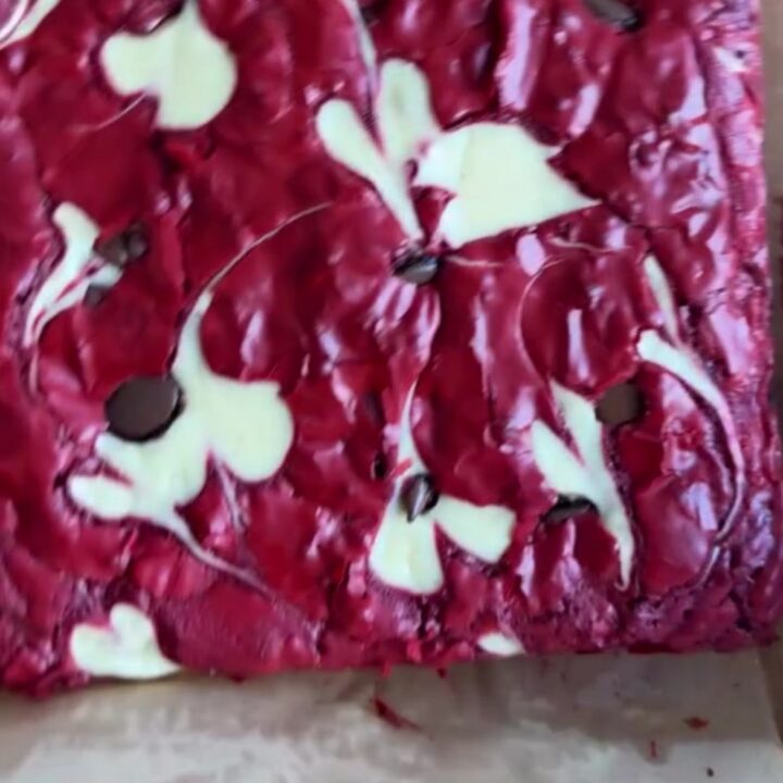 A fudgy red velvet cheesecake brownie slice showing marbled crimson and creamy layers on a white plate.
