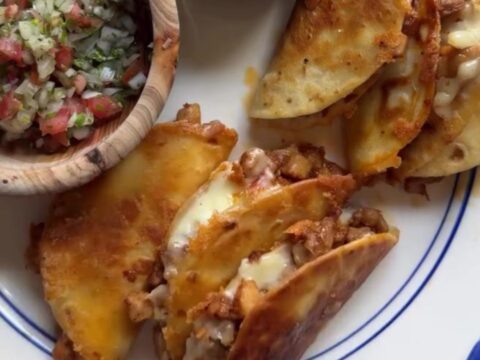 Golden-fried folded chicken tacos topped with pico de gallo and spicy drizzle on a rustic plate