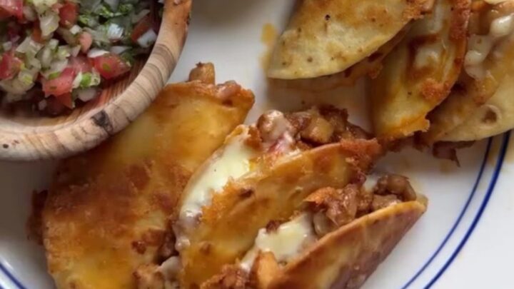 Golden-fried folded chicken tacos topped with pico de gallo and spicy drizzle on a rustic plate