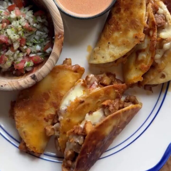 Golden-fried folded chicken tacos topped with pico de gallo and spicy drizzle on a rustic plate