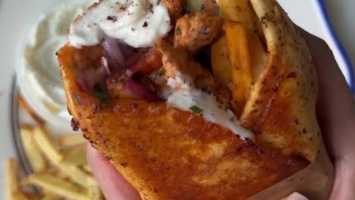 Crispy chicken shawarma wrap sliced in half, showing layers of chicken, fries, onions, and tomatoes