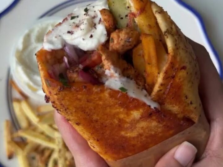 Crispy chicken shawarma wrap sliced in half, showing layers of chicken, fries, onions, and tomatoes