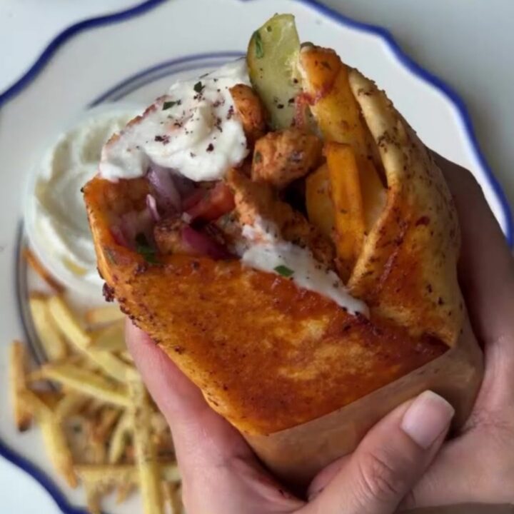 Crispy chicken shawarma wrap sliced in half, showing layers of chicken, fries, onions, and tomatoes
