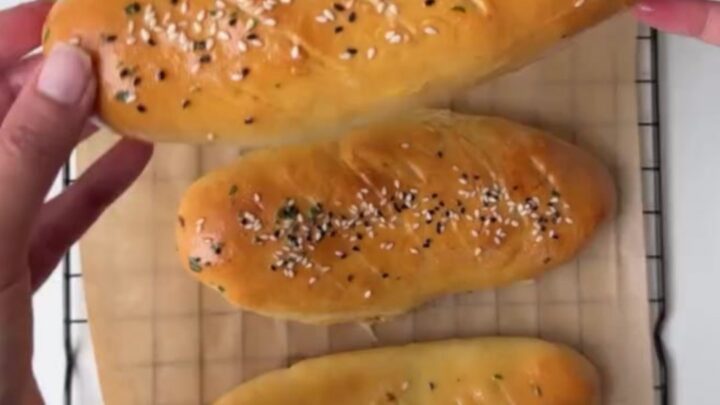 Golden pull-apart rolls on a baking sheet, one torn open with cheese stretching