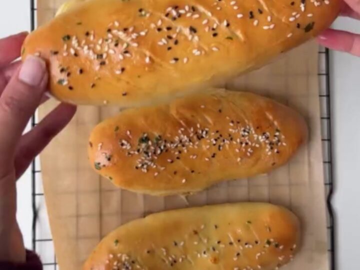 Golden pull-apart rolls on a baking sheet, one torn open with cheese stretching