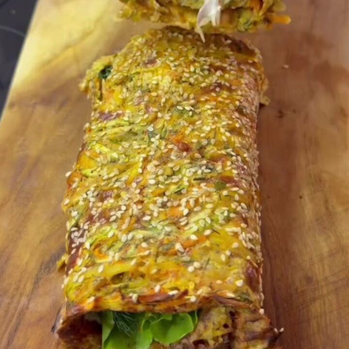 Crispy baked potato roulade sliced into rounds, showing creamy labneh, lettuce, tomato, red onion, and boiled egg layers.