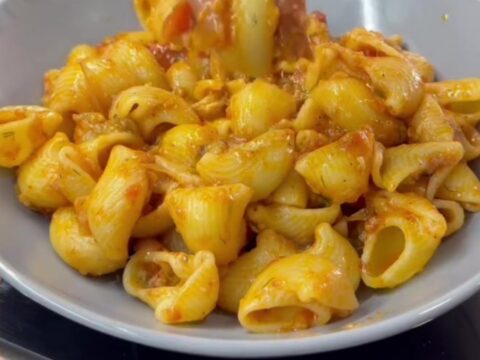 Spoon lifting saucy pipe rigate pasta with melted cheese from a skillet