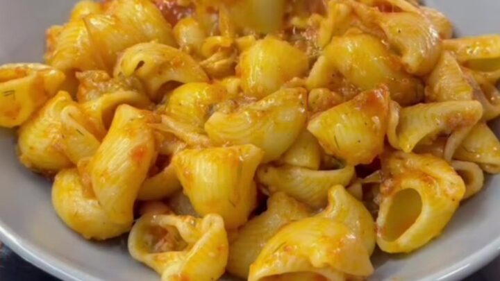Spoon lifting saucy pipe rigate pasta with melted cheese from a skillet
