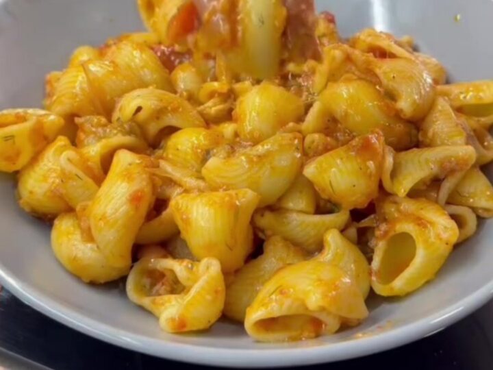 Spoon lifting saucy pipe rigate pasta with melted cheese from a skillet