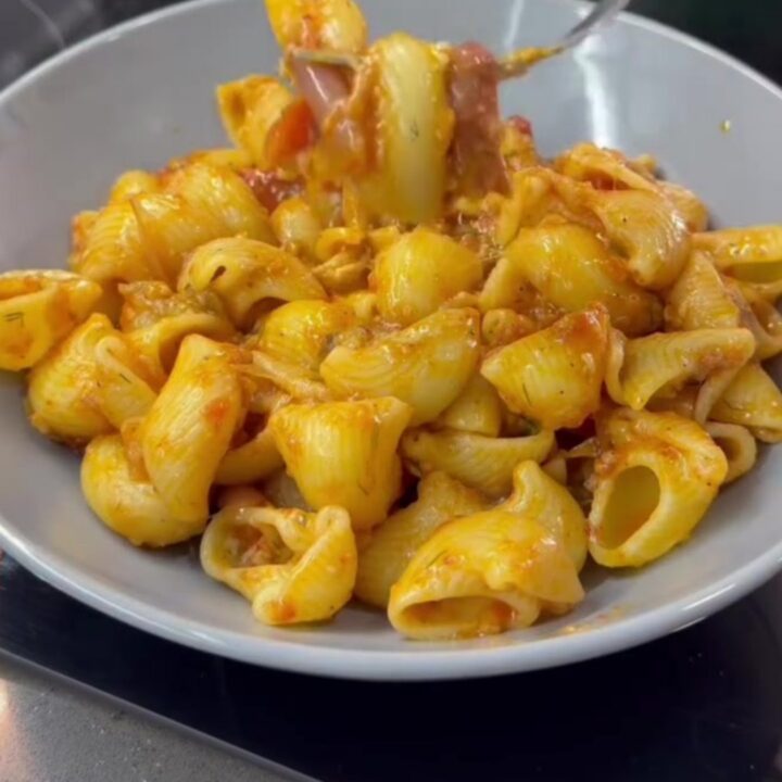 Spoon lifting saucy pipe rigate pasta with melted cheese from a skillet