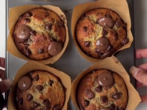 Tall golden banana chocolate chip muffins with melted chocolate chips on top, on a cooling rack