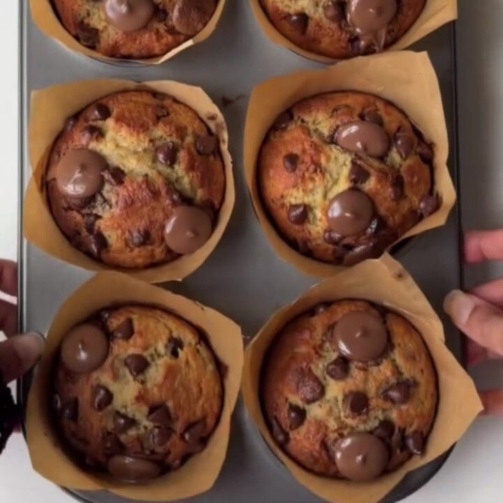 Tall golden banana chocolate chip muffins with melted chocolate chips on top, on a cooling rack
