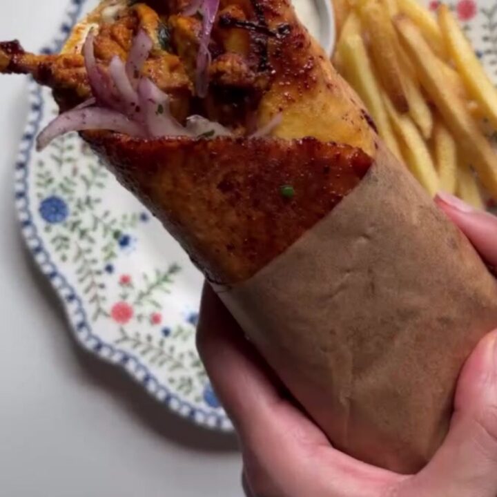Crispy chicken shawarma wrap sliced diagonally, showing layers of chicken, fries, onions, and tomatoes, with a bowl of toum