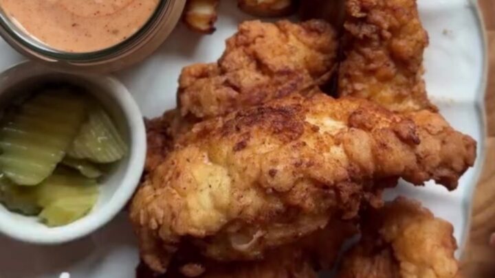 Golden-brown crispy chicken fingers piled on a plate with a bowl of pink sauce for dipping.