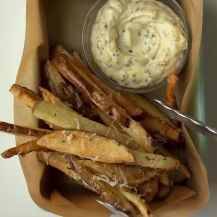 Golden crispy fries tossed with garlic butter, parmesan, and parsley, with a bowl of creamy garlic aioli for dipping.
