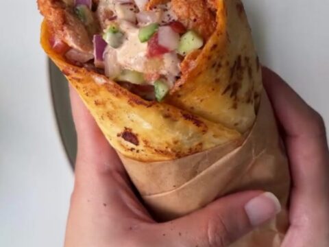 Crispy toasted chicken wrap sliced in half, showing juicy chicken, lettuce, and tomato.