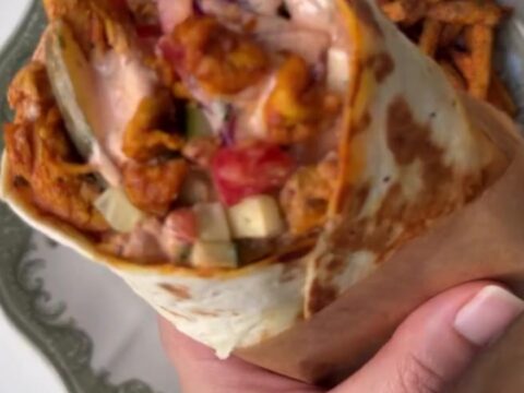 A golden toasted chicken shawarma wrap cut in half, showing spiced chicken, fries, and garlic sauce.